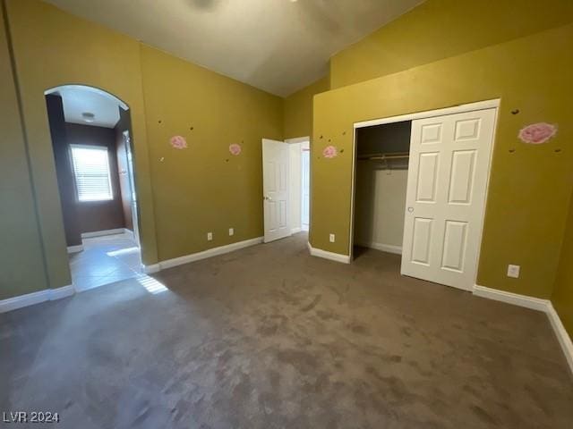 unfurnished bedroom with dark colored carpet, a closet, and lofted ceiling