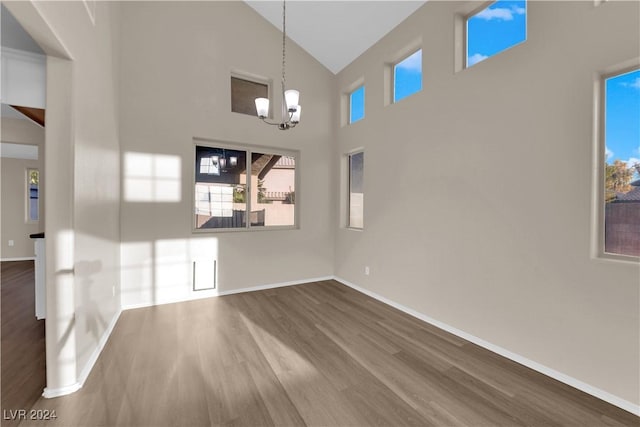 unfurnished living room featuring hardwood / wood-style floors, high vaulted ceiling, and an inviting chandelier