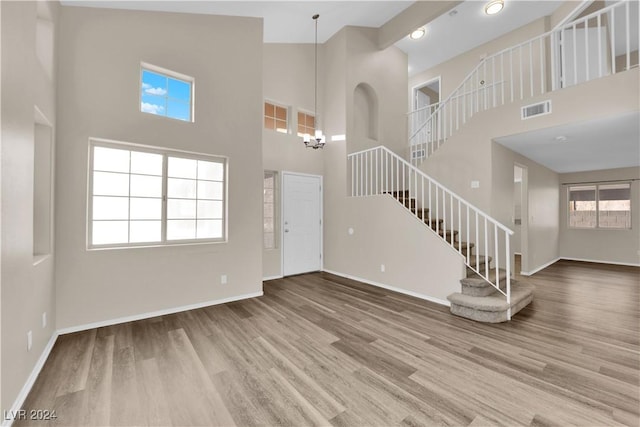 unfurnished living room featuring a towering ceiling, wood-type flooring, and a notable chandelier