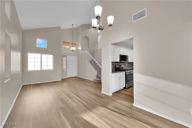 unfurnished living room featuring light hardwood / wood-style flooring, high vaulted ceiling, and a notable chandelier