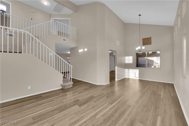 unfurnished living room with hardwood / wood-style floors, a notable chandelier, and a high ceiling