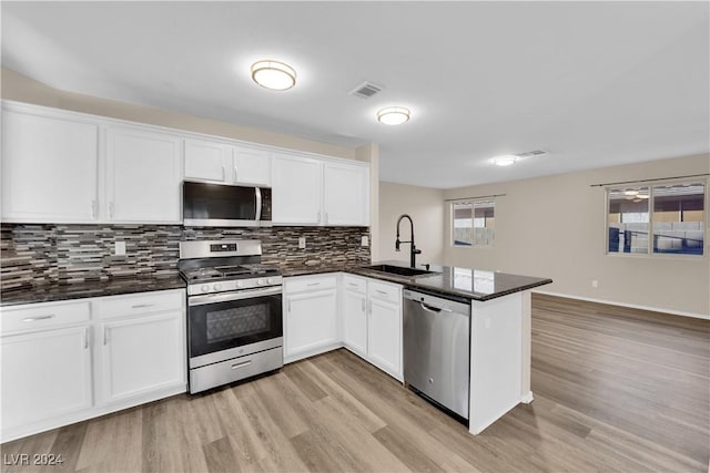 kitchen featuring dark stone counters, kitchen peninsula, sink, appliances with stainless steel finishes, and white cabinetry