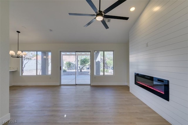 unfurnished living room featuring ceiling fan with notable chandelier, light hardwood / wood-style flooring, and lofted ceiling