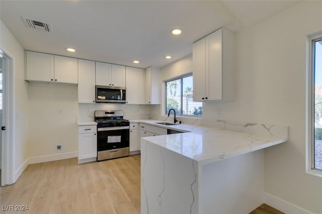 kitchen featuring light stone countertops, white cabinetry, sink, stainless steel appliances, and light hardwood / wood-style flooring