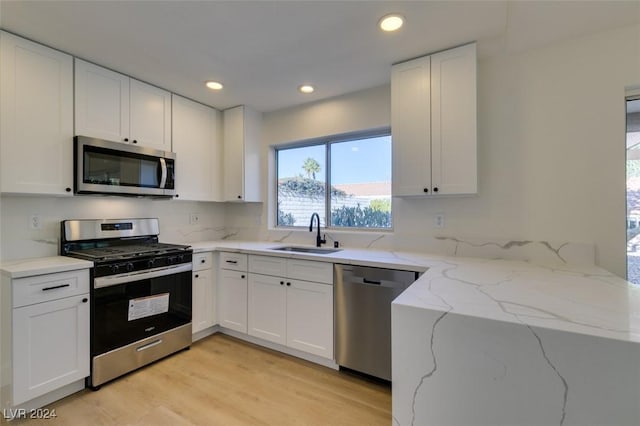 kitchen with light stone countertops, white cabinetry, sink, and stainless steel appliances