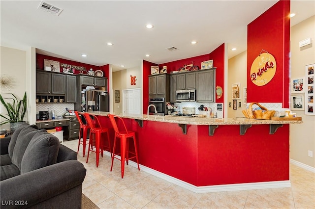 kitchen with a breakfast bar, light tile patterned floors, tasteful backsplash, kitchen peninsula, and stainless steel appliances