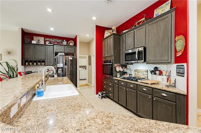 kitchen featuring sink, decorative backsplash, dark brown cabinets, washer / dryer, and stainless steel appliances