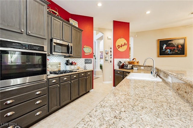 kitchen featuring light stone countertops, appliances with stainless steel finishes, dark brown cabinetry, and sink