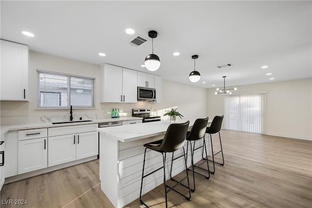 kitchen featuring stainless steel appliances, sink, decorative light fixtures, white cabinets, and a kitchen island