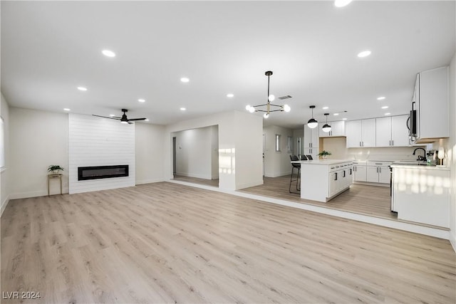 kitchen with a center island, a large fireplace, decorative light fixtures, light hardwood / wood-style floors, and white cabinetry