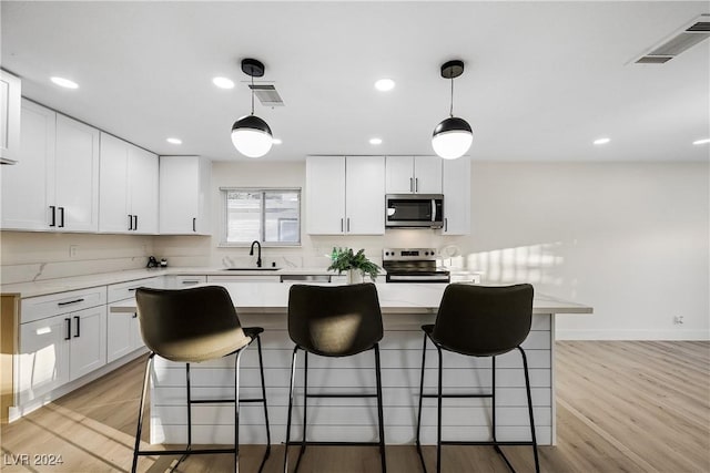 kitchen featuring white cabinetry, sink, light hardwood / wood-style floors, pendant lighting, and appliances with stainless steel finishes