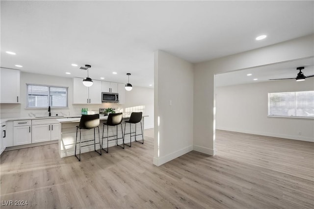 kitchen featuring a kitchen island, pendant lighting, light hardwood / wood-style floors, white cabinetry, and a breakfast bar area