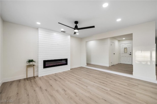 unfurnished living room with ceiling fan, a large fireplace, and light wood-type flooring