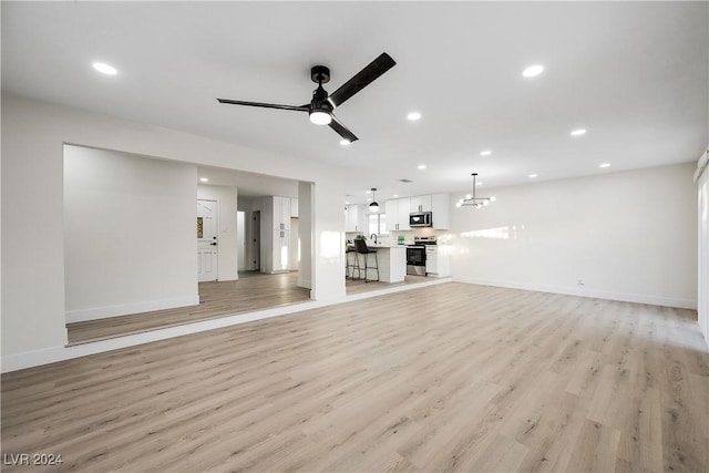 unfurnished living room with ceiling fan with notable chandelier and light wood-type flooring