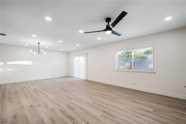 spare room featuring ceiling fan with notable chandelier and light wood-type flooring