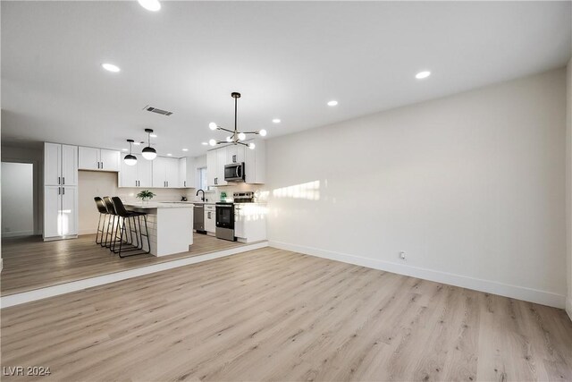 kitchen featuring hanging light fixtures, light hardwood / wood-style flooring, appliances with stainless steel finishes, a kitchen island, and white cabinetry