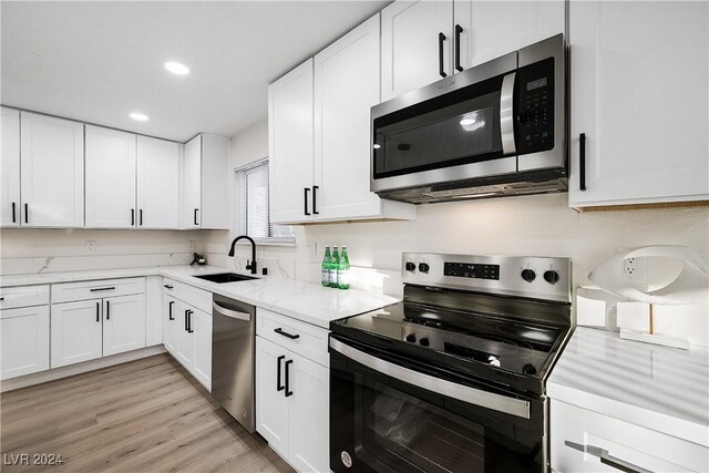 kitchen featuring light stone countertops, appliances with stainless steel finishes, sink, white cabinets, and light hardwood / wood-style floors