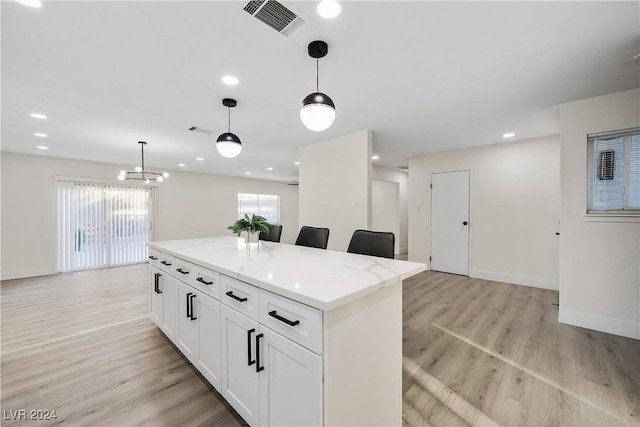 kitchen featuring a center island, white cabinets, hanging light fixtures, light stone countertops, and light wood-type flooring