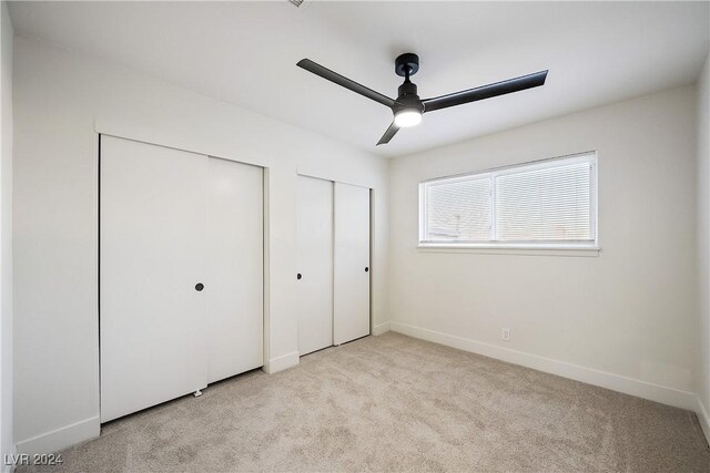 unfurnished bedroom featuring multiple closets, light carpet, and ceiling fan