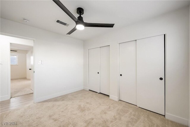 unfurnished bedroom featuring light colored carpet, ceiling fan, and multiple closets