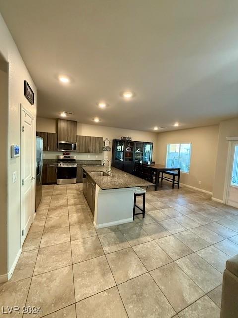 kitchen featuring light tile patterned floors, sink, a breakfast bar, appliances with stainless steel finishes, and a center island with sink