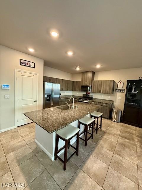 kitchen featuring appliances with stainless steel finishes, sink, dark stone countertops, a kitchen bar, and a kitchen island with sink