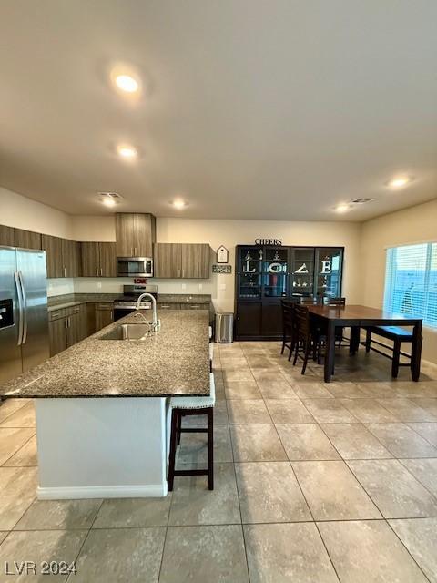 kitchen with appliances with stainless steel finishes, sink, a kitchen breakfast bar, light stone countertops, and a center island with sink