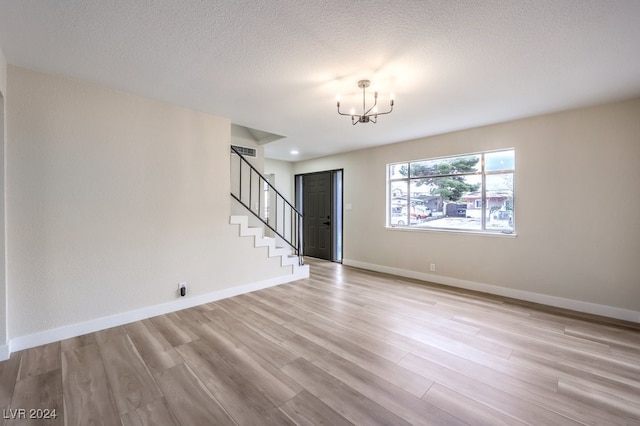 unfurnished living room featuring light hardwood / wood-style floors, a textured ceiling, and an inviting chandelier