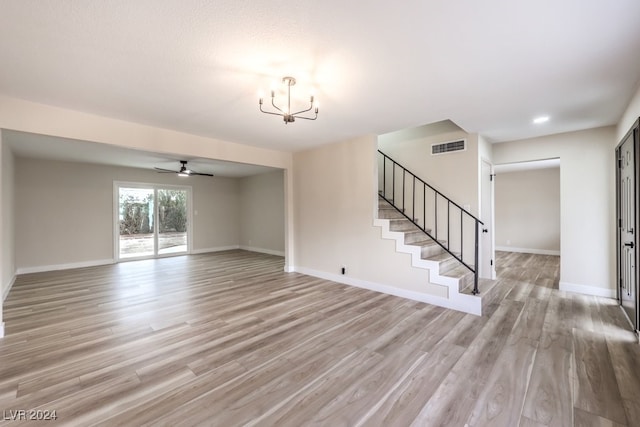 unfurnished living room with ceiling fan with notable chandelier and light hardwood / wood-style floors