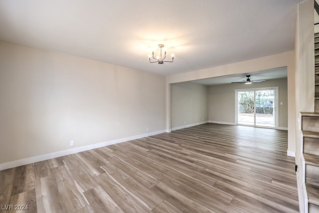 unfurnished living room with ceiling fan with notable chandelier and light hardwood / wood-style floors