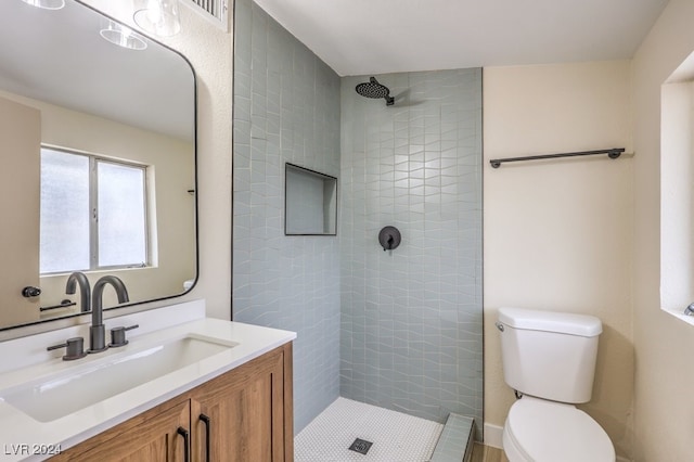 bathroom with a tile shower, vanity, and toilet