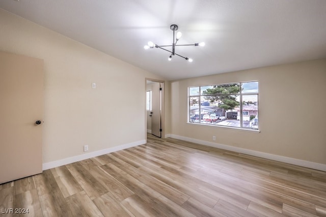 empty room featuring a chandelier, light hardwood / wood-style floors, and lofted ceiling