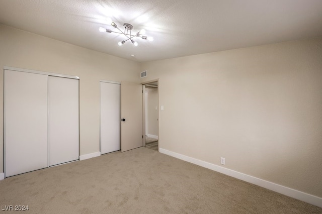 unfurnished bedroom with carpet flooring, a chandelier, and two closets