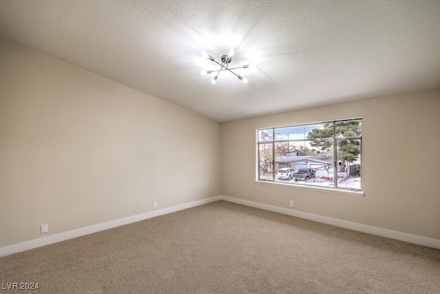 carpeted spare room featuring a chandelier and a textured ceiling