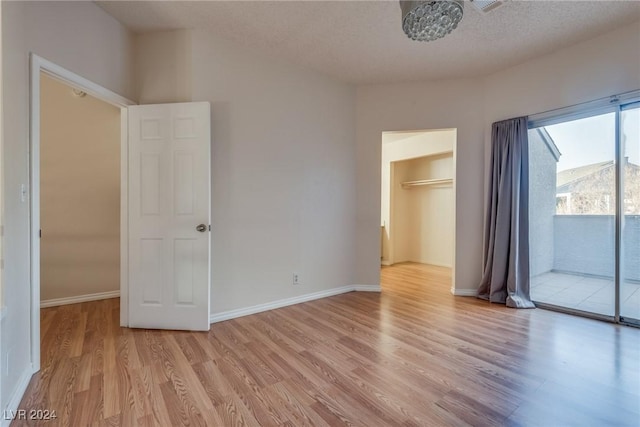 unfurnished bedroom featuring a spacious closet, a closet, light hardwood / wood-style floors, and a textured ceiling