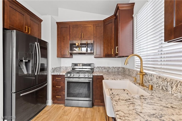 kitchen featuring light stone countertops, appliances with stainless steel finishes, light hardwood / wood-style flooring, and lofted ceiling