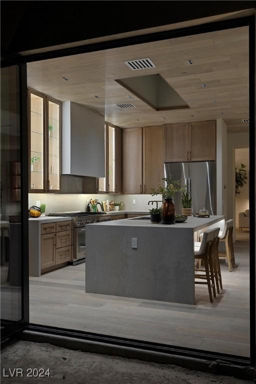 kitchen with wall chimney exhaust hood, appliances with stainless steel finishes, a kitchen island, and visible vents