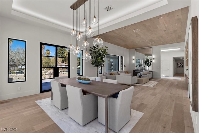 dining room featuring light wood finished floors, baseboards, visible vents, and a raised ceiling