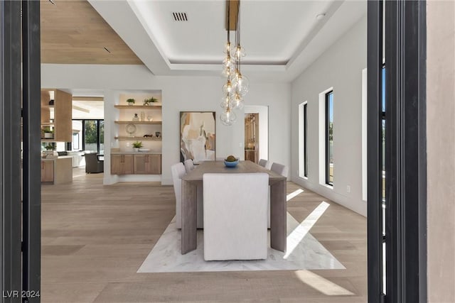 dining room featuring visible vents, a raised ceiling, built in features, light wood-type flooring, and a chandelier