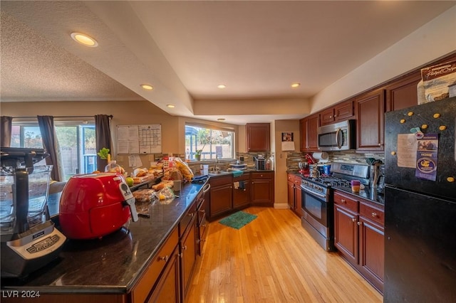 kitchen with dark stone countertops, decorative backsplash, light hardwood / wood-style flooring, and appliances with stainless steel finishes