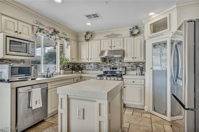 kitchen with sink, a center island, backsplash, light stone countertops, and appliances with stainless steel finishes