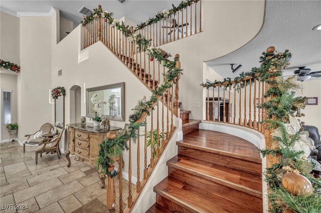 stairs featuring a towering ceiling, ceiling fan, and crown molding