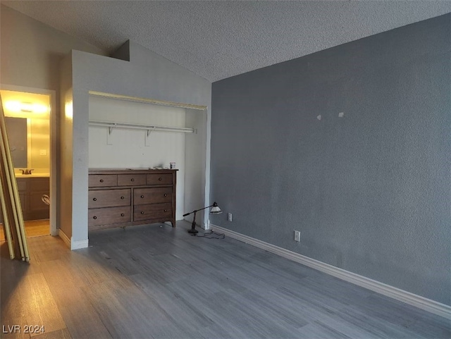 unfurnished bedroom with a textured ceiling, a closet, lofted ceiling, and light hardwood / wood-style flooring