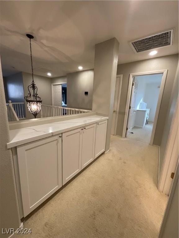 kitchen featuring pendant lighting, light colored carpet, and white cabinetry