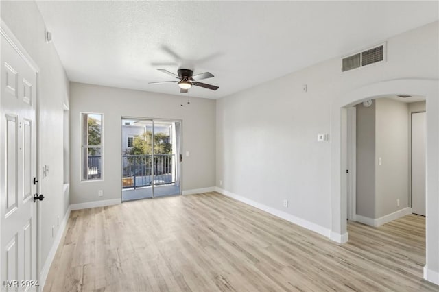 spare room featuring light wood-style floors, visible vents, arched walkways, and a ceiling fan