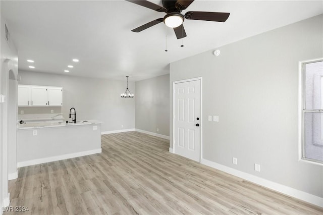 unfurnished living room with light wood-style flooring, baseboards, a sink, and ceiling fan with notable chandelier