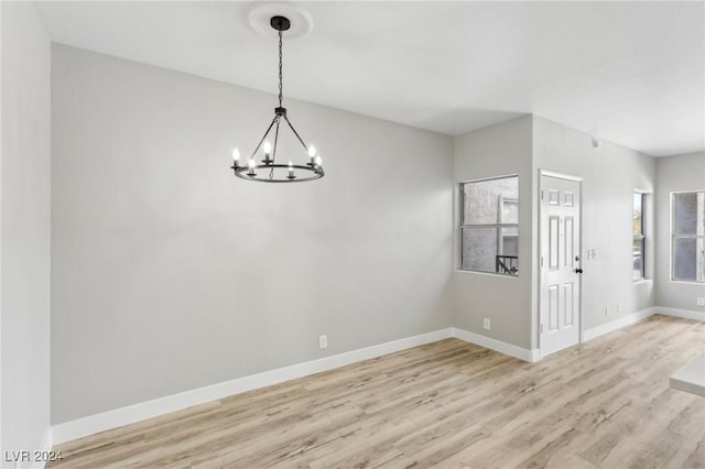 spare room featuring a notable chandelier, light wood-style flooring, and baseboards