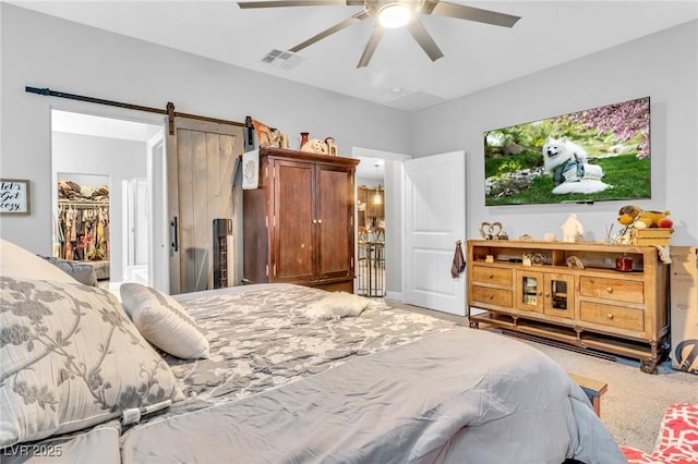 carpeted bedroom with a barn door, ceiling fan, a closet, and a walk in closet