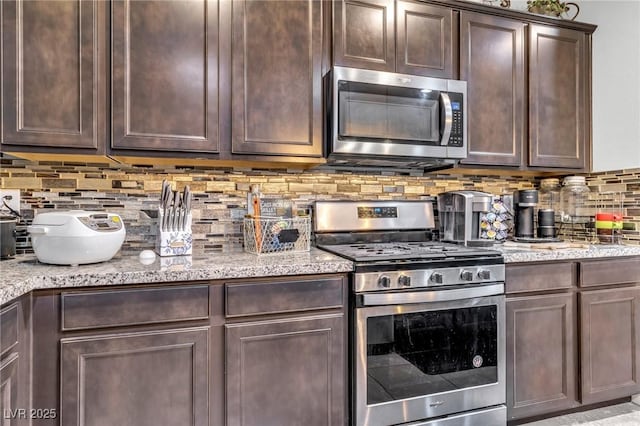 kitchen with decorative backsplash, appliances with stainless steel finishes, dark brown cabinetry, and light stone counters