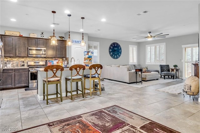 kitchen with backsplash, a center island with sink, a breakfast bar area, decorative light fixtures, and stainless steel appliances